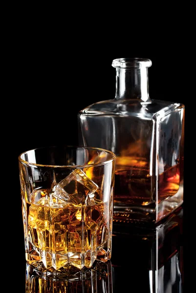 Faceted glass of whiskey with ice and a bottle — Stock Photo, Image