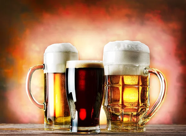 Mugs and glass of beer on a wooden table — Stock Photo, Image