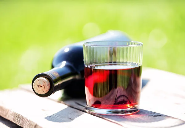 Copo de vinho tinto e garrafa deitada na mesa de madeira — Fotografia de Stock