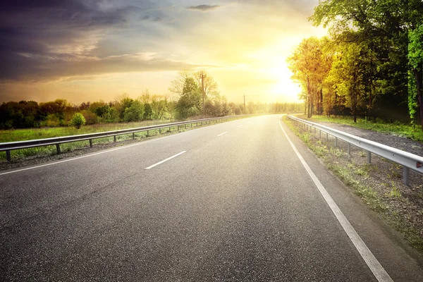 Estrada de asfalto saindo para virar para o sol — Fotografia de Stock