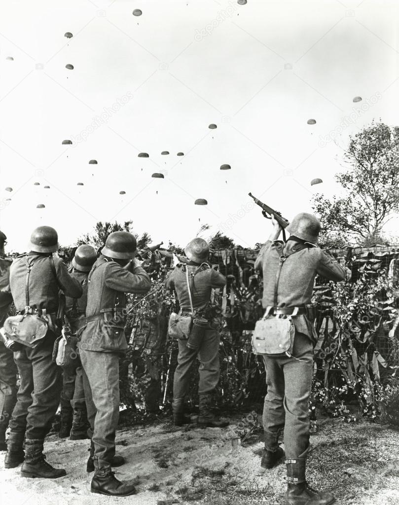 Soldiers shooting at enemy parachuting into field