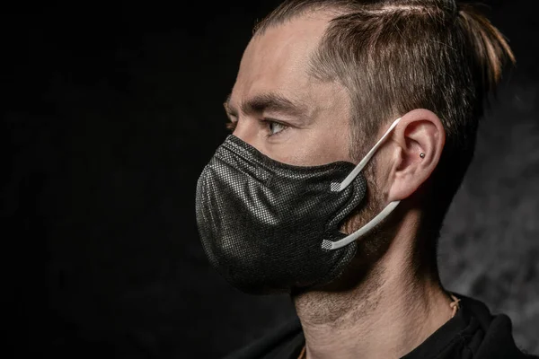 Een man met een zwart masker op zijn gezicht op een donkere achtergrond in de studio — Stockfoto