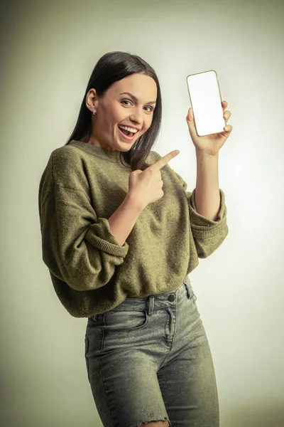 Glada söt kvinna pekar finger på smartphone skärmen. Titta på kameran — Stockfoto