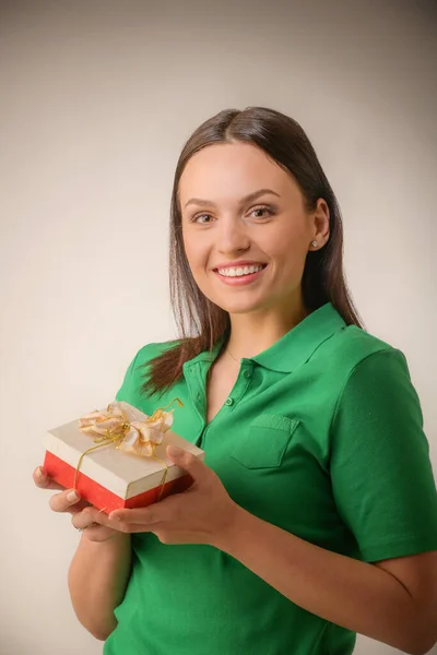 Jonge vrouw portret houden geschenk in kerst kleur stijl. Glimlachend gelukkig meisje op een lichtgrijze achtergrond — Stockfoto