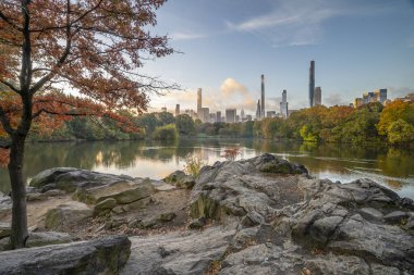 Central Park, New York City 'deki gölde sonbaharda sabahın erken saatlerinde dramatik bir gökyüzü ile Manhattan' da.