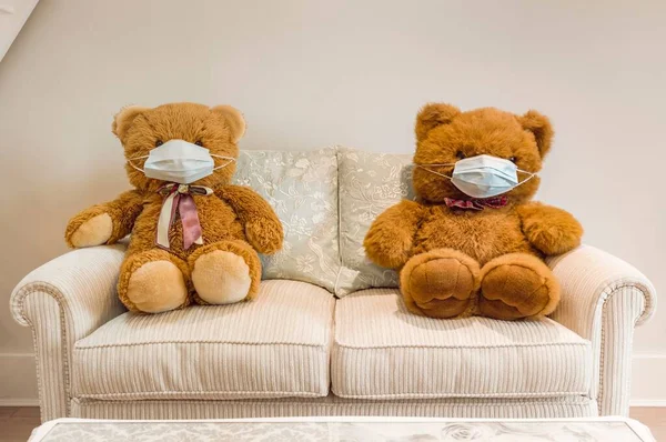 Teddy bears wearing face masks sitting on a sofa, social distancing. Ideal for children, COVID-19 coronavirus social distancing concept.