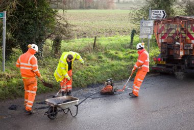 BUCKINGHAM, İngiltere - 14 Aralık 2020. Yol çalışmaları, yol ekibi, yüksek görüş mesafesi olan turuncu elbiseli adamlar. Kırsal bir yoldaki çukurları onarıyor.
