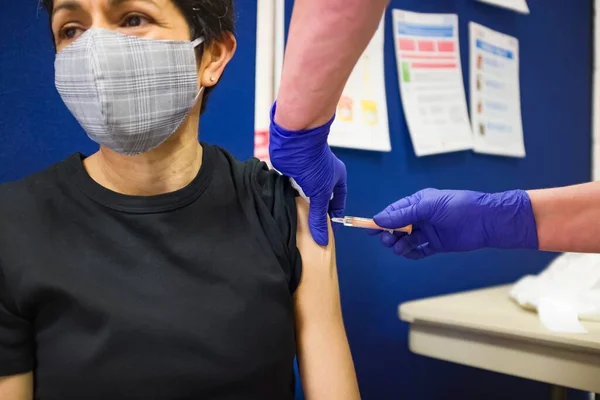 British Asian woman wearing a face mask, getting a Covid 19 vaccine at a vaccination centre in England, UK