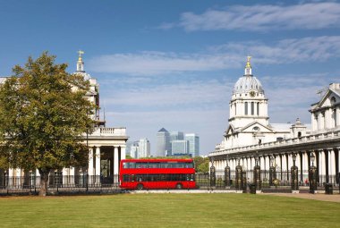 Londra 'nın merkezinde kırmızı çift katlı bir otobüs. Eski Kraliyet Donanma Koleji ve Greenwich Park 'taki Ulusal Denizcilik Müzesi. Canary Wharf silueti