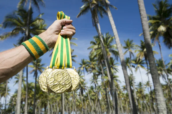 Hånd fra olympiske idrettsutøvere som holder gullmedaljer i palmetrær – stockfoto