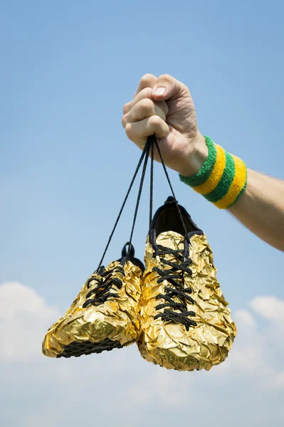 Mano del atleta sosteniendo zapatos de carrera de oro — Foto de Stock