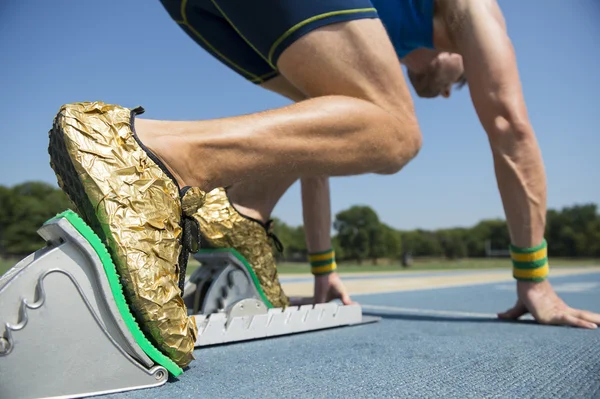 Idrottsman i guld skor på startblocken — Stockfoto