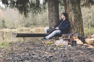 Bitkin gezgin genç adam durgun bir orman gölü kampında uyuyor. 