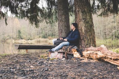 Bitkin gezgin genç adam durgun bir orman gölü kampında uyuyor. 