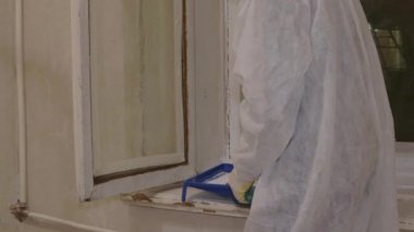 Koruyucu takım elbiseli bir boyacı solunum eldivenleri camları boyuyor. 