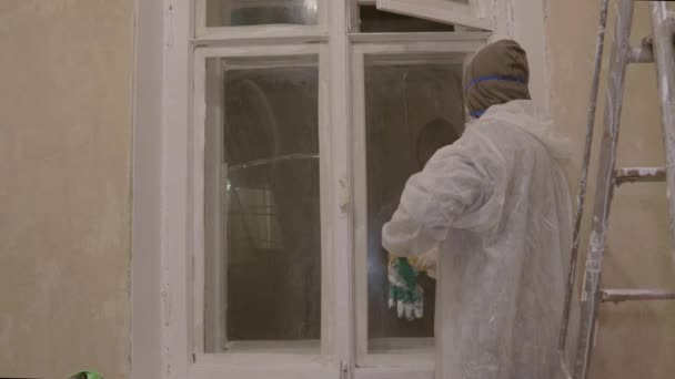 Painter in protective suit respirator gloves paints windows brush — Stock Video