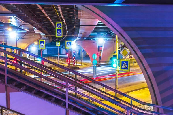 Crossroads traffic lights glowing at night and aboveground pedestrian crossing city transportation interchange .dynamic traffic .concept urban infrastructure . purple magenta multicolors