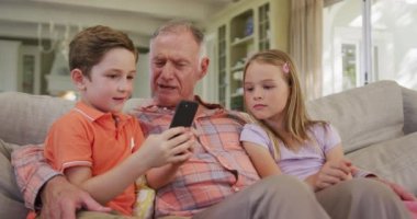 Kafkasyalı kıdemli bir adam, torunu ve torunu evde birlikte vakit geçiriyorlar, oturma odasında bir kanepede oturuyorlar, akıllı telefon kullanıyorlar, ağır çekimde..