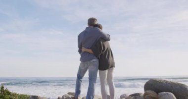 Güneşli bir günde, yavaş çekimde kucaklaşan beyaz bir çift deniz kenarında boş zamanın tadını çıkarıyor. Sahilde erken emeklilik.