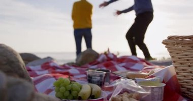 Kafkasyalı çift güneşli bir günde deniz kenarında boş zamanlarını ön planda ağır çekimde battaniyeyle kucaklaşarak geçiriyorlar. Sahilde erken emeklilik.