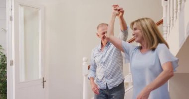 Üst düzey beyaz çift evde birlikte vakit geçiriyorlar, koridorda dans ediyorlar, birbirlerine bakıp gülümsüyorlar, ağır çekimde..