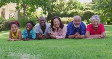 Çoklu nesil Afro-Amerikan aile portresi bahçede birlikte zaman geçiriyorlar, çimlerin üzerinde uzanıyorlar, kameraya bakıp gülümsüyorlar, ağır çekimde..