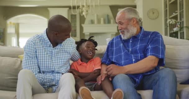 老非洲裔美国人 他的儿子和孙子一起呆在家里 坐在客厅的沙发上 慢吞吞地谈着笑着 — 图库视频影像