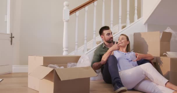白种人夫妇搬进新屋 坐在地上 彼此交谈着 慢吞吞地笑着 四周都是纸板箱 — 图库视频影像