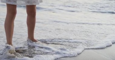 Kumsalda çıplak ayakla yürüyen beyaz bir kadın, deniz kenarında eğleniyor. Boş zaman ve tatil.