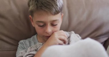 Beyaz çocuk yalnız zaman geçiriyor, kanepede uzanıyor, burnunu mendille siliyor. Covid 19 koronavirüs karantina süresince sosyal mesafeler.