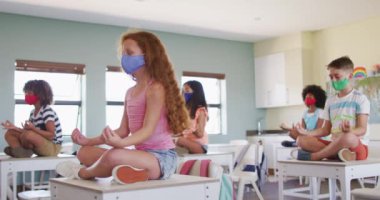 Yüz maskesi takan, masalarda oturup meditasyon yapan çok ırklı bir grup öğrenci. Eğitim, Covid19 Coronavirus salgını sırasında sağlık güvenliğine geri döndü