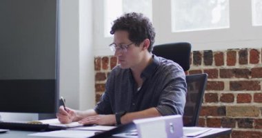 Kafkas erkek iş dünyasının yaratıcı portresi, modern ofiste çalışıyor, masada oturuyor, kameraya bakıyor, ağır çekimde. Yaratıcı iş modern ofis.