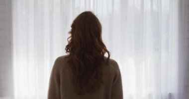 Kafkas kadının evde, oturma odasında, perdeleri yavaş çekimde hareket ettirirken görüntüsü. Covid 19 Coronavirus karantina süresince sosyal mesafeler.