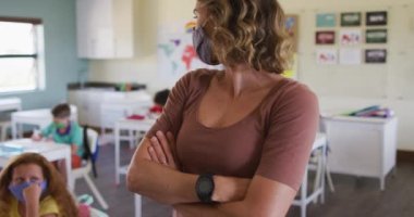 Okulda yüz maskesi takan beyaz kadın öğretmen, okulda çocuklara ders veriyor. Eğitim, Covid19 Coronavirus salgını sırasında sağlık güvenliğine geri döndü.