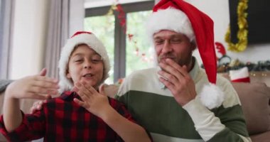 Beyaz bir adam oğluyla birlikte vakit geçiriyor, bir koltukta oturuyor, Noel 'i kutluyor, öpüşüyor ve el sallıyor. Covid 19 koronavirüs karantina süresince sosyal mesafeler.