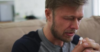 Kafkasyalı bir adam kanepeye oturup mendile hapşırarak vakit geçiriyor. Covid 19 koronavirüs karantina süresince sosyal mesafeler.