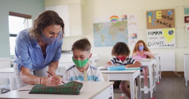 白人女性教師は学校でフェイスマスクを着用し 学校の教室で子供たちに教える Covi19コロナウイルスパンデミックの際の学校の安全性への教育 — ストック動画