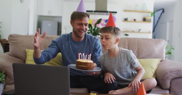 白人男人花时间和他的儿子在一起 坐在沙发上 庆祝儿子的生日 拿着生日蛋糕 用笔记本电脑 食环动物检疫期间的社会疏离 — 图库视频影像