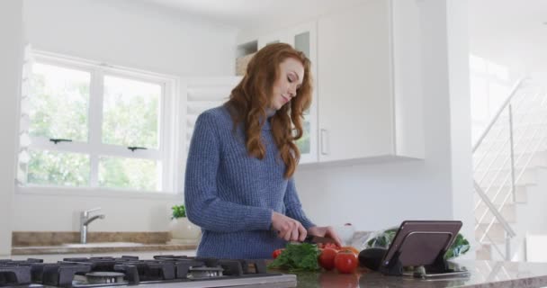 家庭で過ごす白人女性 台所で野菜を切り刻む スローモーションで彼女のデジタルタブレットを使用して Covid 19コロナウイルス隔離ロックダウン中の社会的距離 — ストック動画