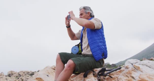 Hombre Senderista Mayor Sentado Las Rocas Las Montañas Tomando Fotos — Vídeo de stock