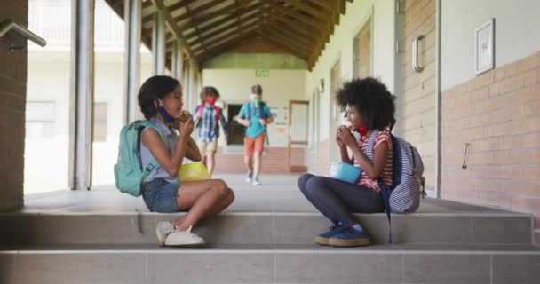 学校の子供たちの顔のマスクを着て 階段に座って朝食を食べるの複数の民族グループ Covi19コロナウイルスパンデミックの際の学校の安全性への教育 — ストック動画