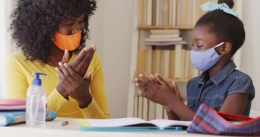 Afrika kökenli Amerikalı anne ve kız yüz maskesi takıp ellerini evde sterilize ediyorlar. Covid 19 koronavirüs karantina süresince sosyal mesafeler.