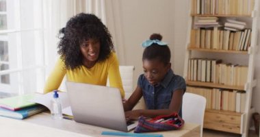 Afrika kökenli Amerikalı anne ve kız birbirlerine bakıp gülümserken evde otururken dizüstü bilgisayar kullanıyorlar. Covid 19 koronavirüs karantina süresince sosyal mesafeler.