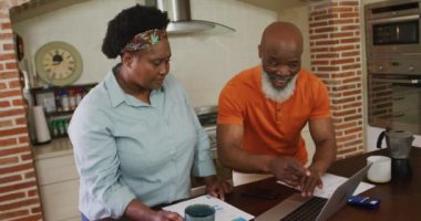 Mutlu Afro-Amerikan son sınıf çifti evdeki mutfakta dizüstü bilgisayar kullanıyor. Koronavirüs salgını sırasında karantina karantinasına sosyal uzaklık