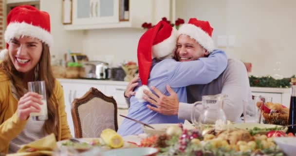 白种人的老妇人头戴圣诞礼帽 一边抱着儿子 一边坐在饭桌上 一边在家里共进午餐 圣诞节庆祝传统的概念 — 图库视频影像