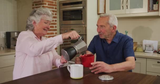 Idősebb Kaukázusi Házaspár Otthon Konyhában Ülve Reggelizik Kávét Tölt Mosolyog — Stock videók