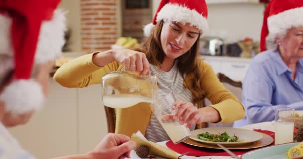 白种人女人头戴圣诞礼帽 坐在餐桌旁 在家中共进午餐时 把饮料倒入老年人的杯子里 圣诞节庆祝传统的概念 — 图库视频影像