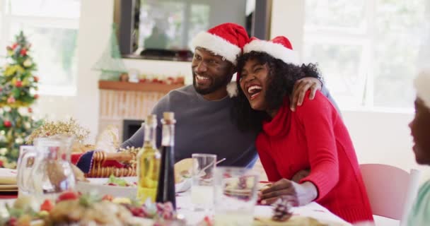Afroamerikanisches Paar Mit Weihnachtsmannmützen Lächelt Und Prostet Während Esstisch Sitzt — Stockvideo