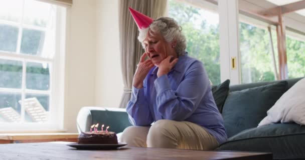 自宅で窓の外を見て誕生日ケーキと悲しい原因アジアのシニア女性 コロナウイルスの隔離中の社会的距離 — ストック動画