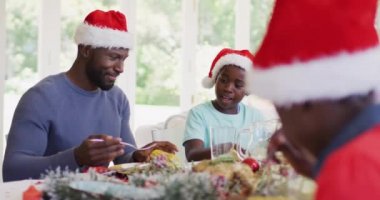 Afrikalı Amerikalı baba oğlunun tabağında yemek servisi yapıyor. Noel 'de birlikte yemek masasında oturup öğle yemeği yiyorlar. Noel bayramı geleneği kutlaması